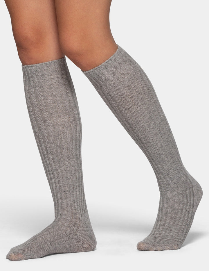 A model wearing a pair of light gray ribbed knee-high socks on a light gray background.