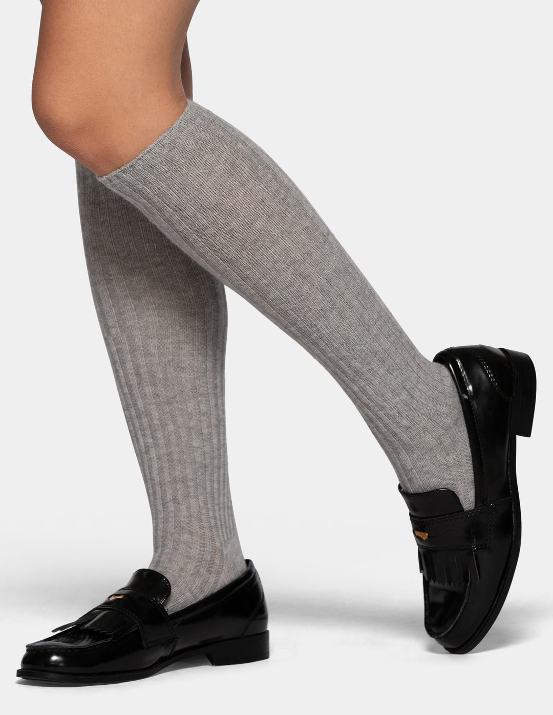A model wearing a pair of light gray ribbed knee-high socks on a light gray background.