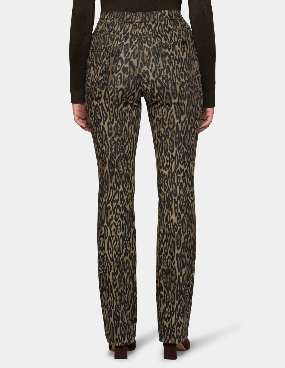 A backside view of a model wearing olive leopard print leggings and a long sleeve dark color top, paired with dark brown suede boots against a light gray background.