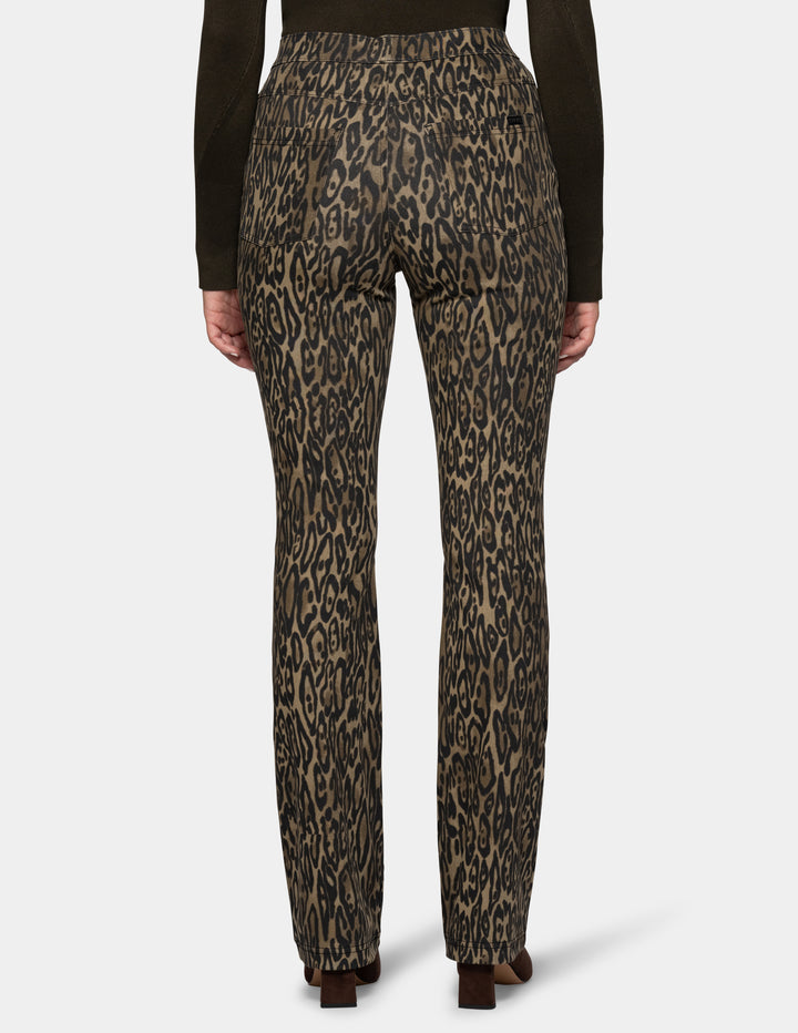 A backside view of a model wearing olive leopard print leggings and a long sleeve dark color top, paired with dark brown suede boots against a light gray background.