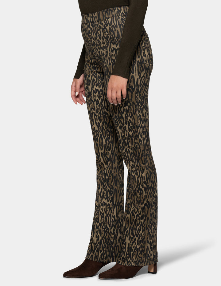 A sideview of a model wearing olive leopard print leggings and a long sleeve dark color top, paired with dark brown suede boots against a light gray background.