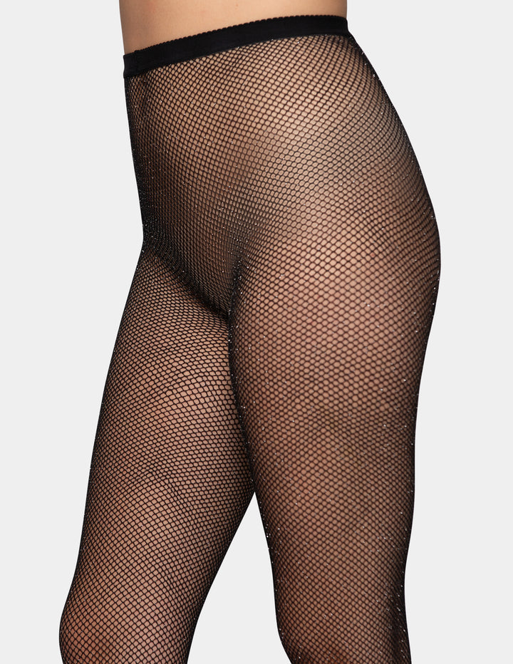 A detailed view of a model wearing black fishnet tights photographed against a light gray background.
