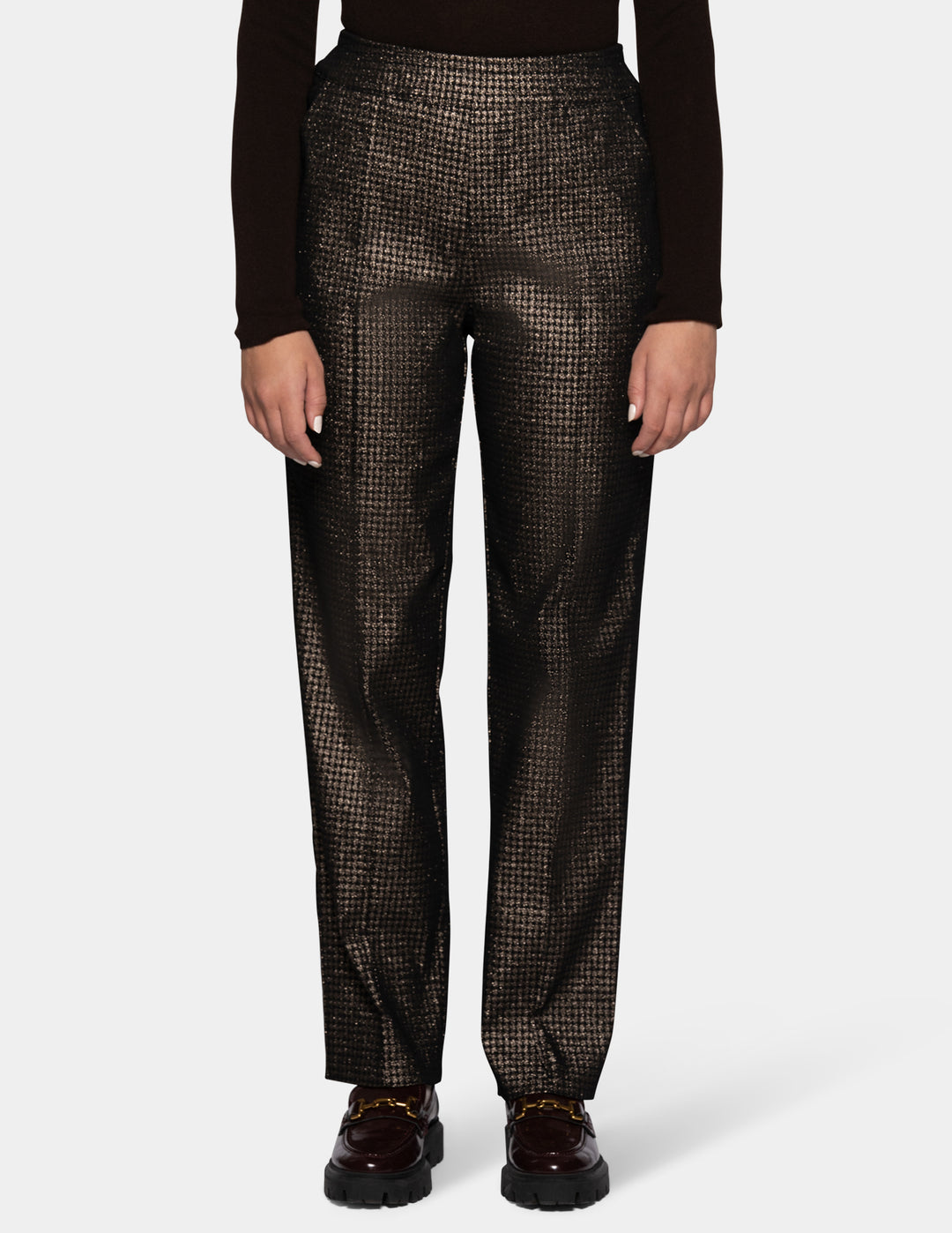 A model wearing metallic trousers and a long sleeve black shirt with dark color loafers.