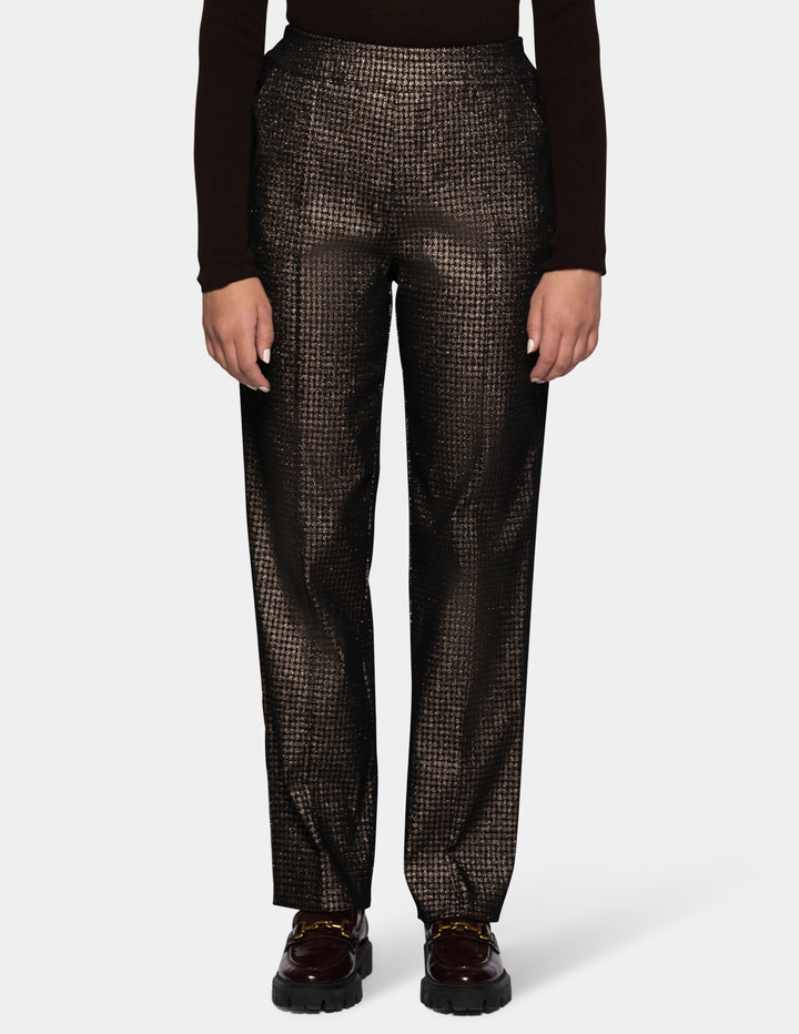 A model wearing metallic trousers and a long sleeve black shirt with dark color loafers.