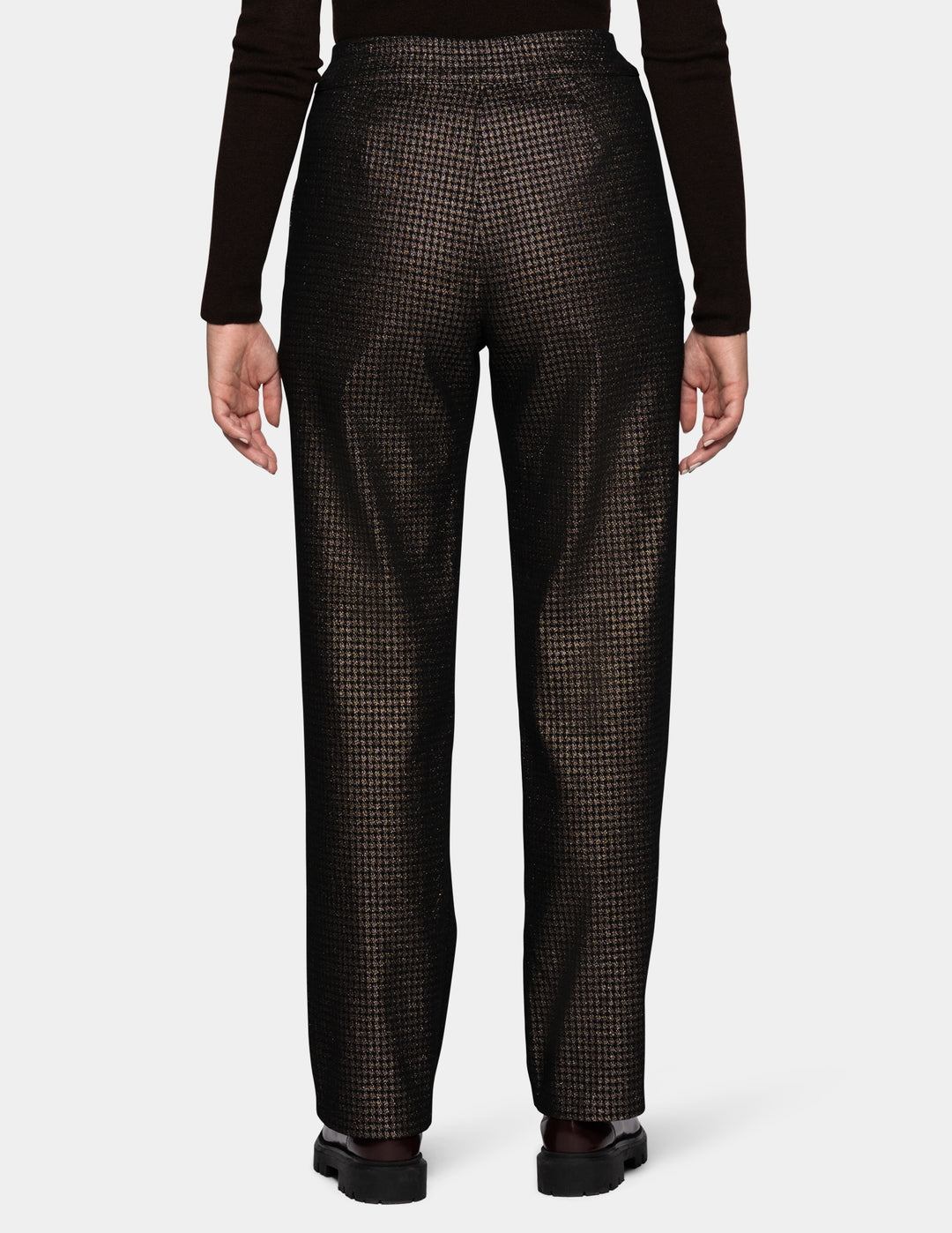 A backside view of a model wearing metallic trousers and a long sleeve black shirt with dark color loafers.