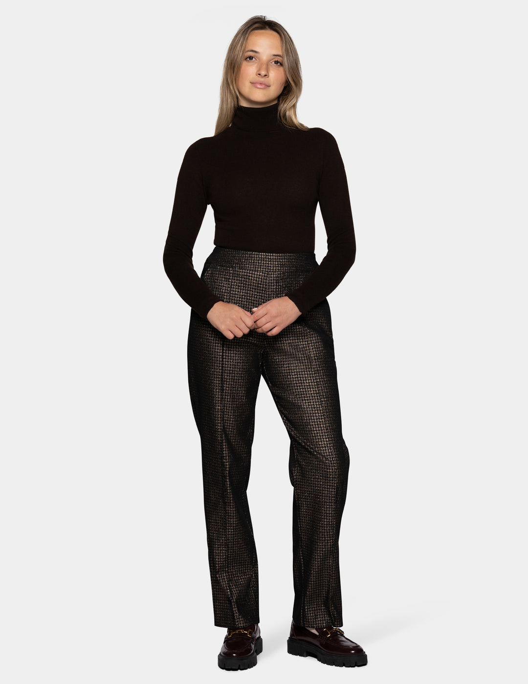 A model wearing metallic trousers and a long sleeve black shirt with dark color loafers.
