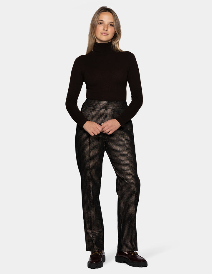 A model wearing metallic trousers and a long sleeve black shirt with dark color loafers.