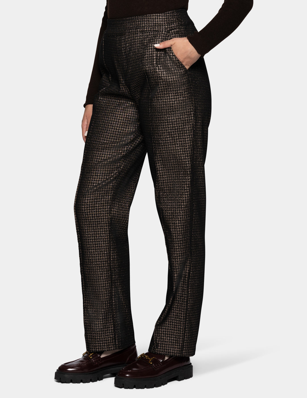 A sideview of a model wearing metallic trousers and a long sleeve black shirt with dark color loafers.