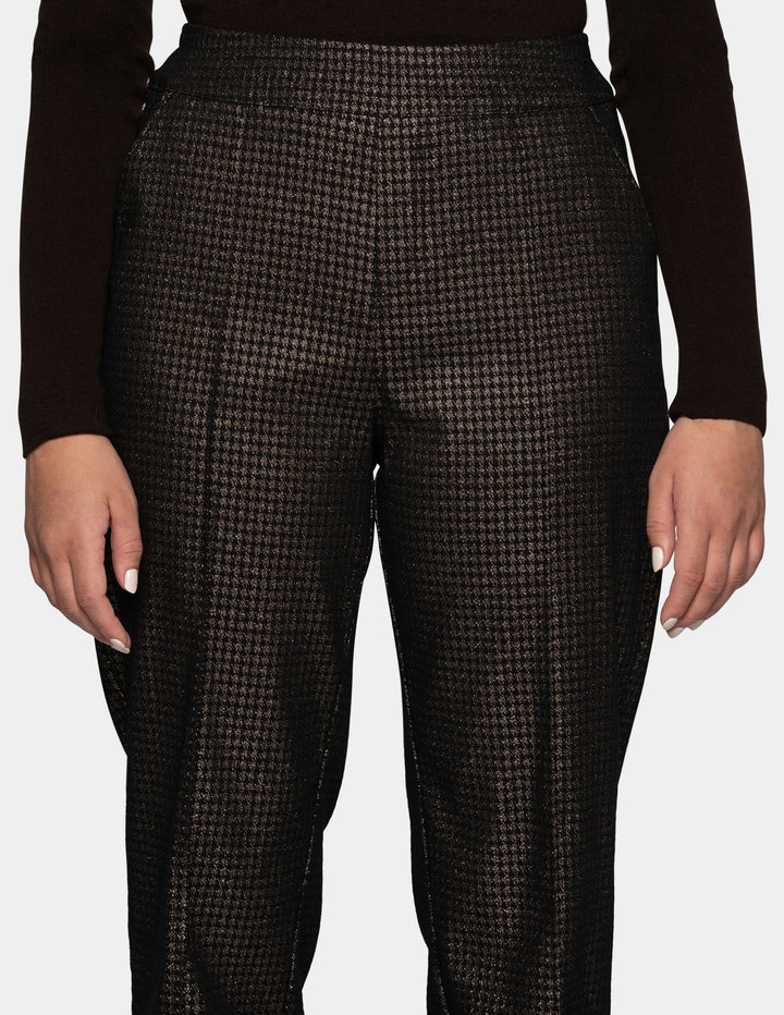 A model wearing metallic trousers and a long sleeve black shirt.