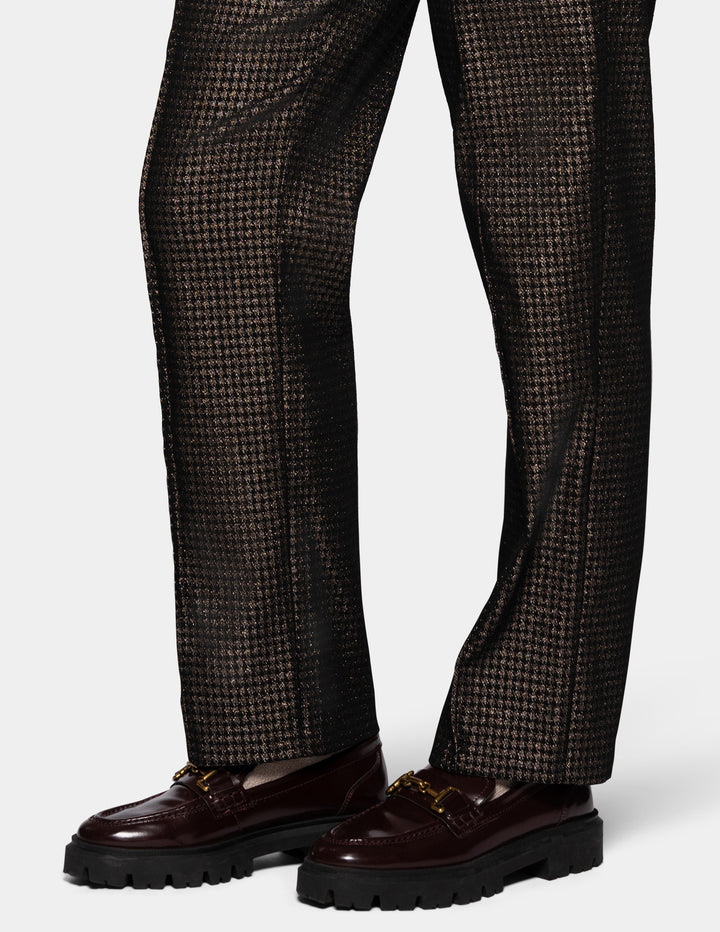 A model wearing metallic trousers with dark color loafers.