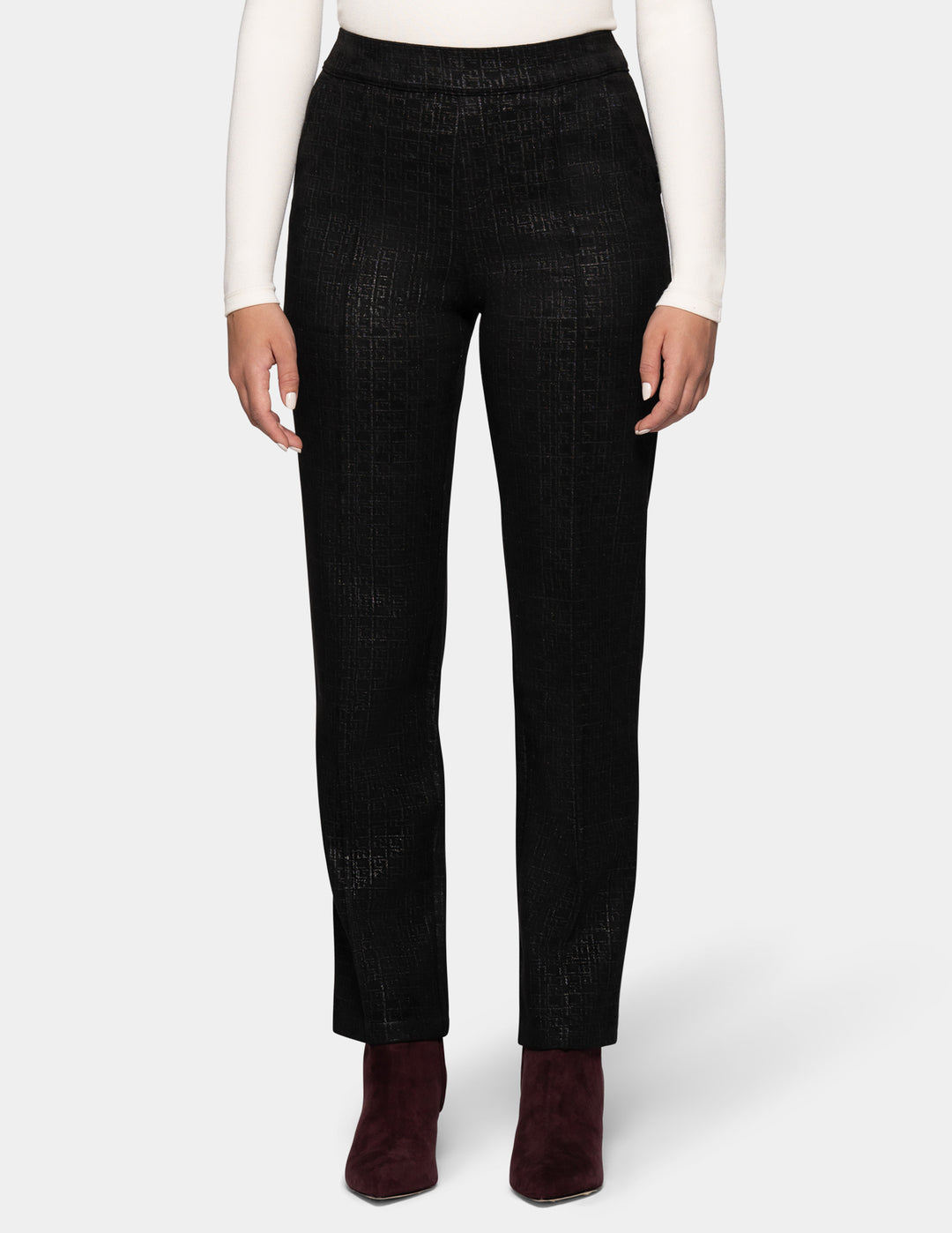 A model is shown from the waist down wearing black textured trousers, a white long-sleeve top, and dark burgundy ankle boots, set against a plain light gray studio background.