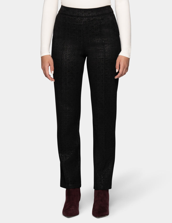 A model is shown from the waist down wearing black textured trousers, a white long-sleeve top, and dark burgundy ankle boots, set against a plain light gray studio background.