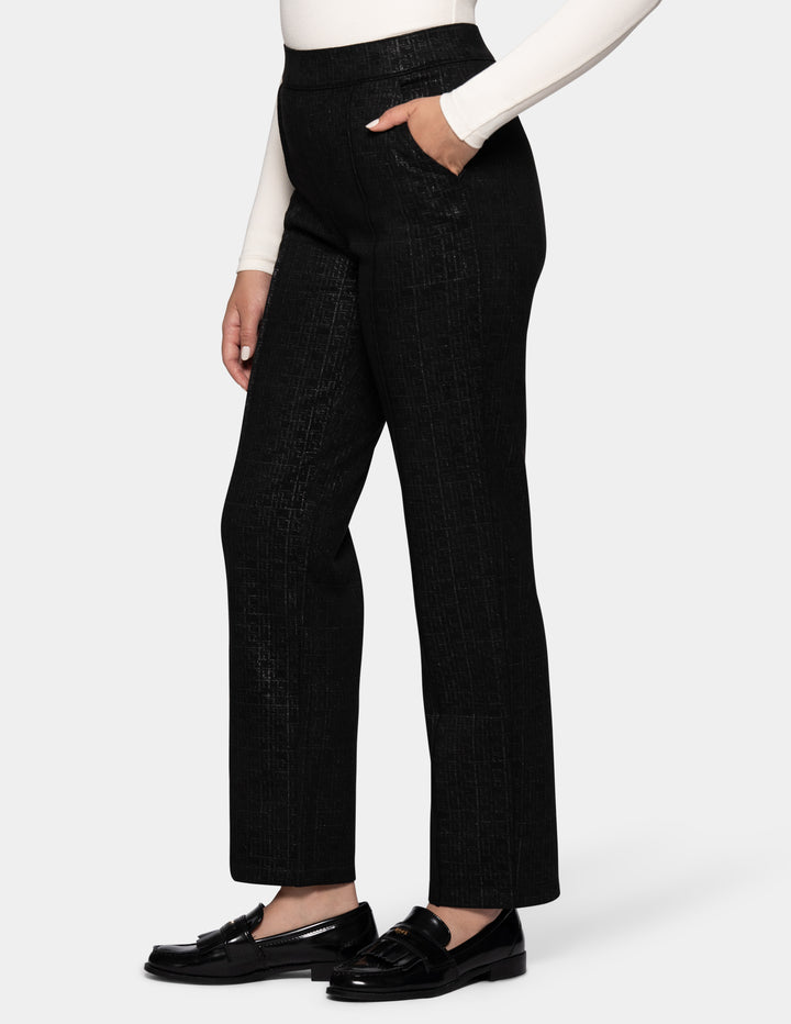 A side view of a model wearing black textured trousers, a white long-sleeve top, and black loafers, set against a plain light gray studio background.