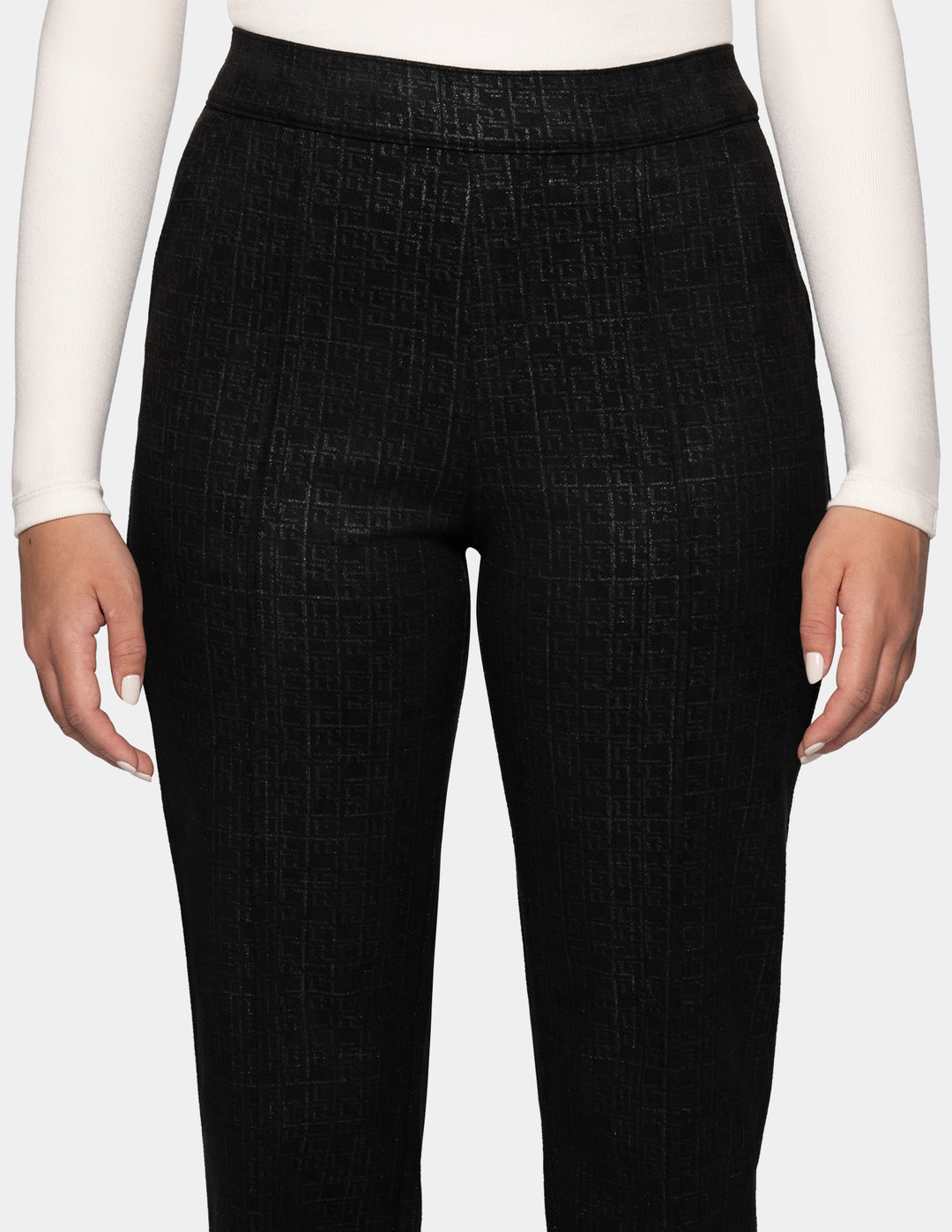 A close-up view of a model wearing black textured trousers, and a white long-sleeve top, set against a plain light gray studio background.