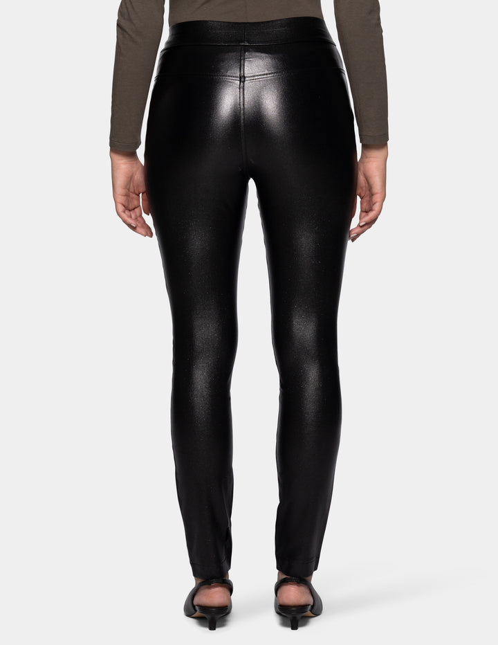 A backside view of a model wearing coated black pants, a grey 3/4 sleeve top, and black flats photographed against a light gray background.