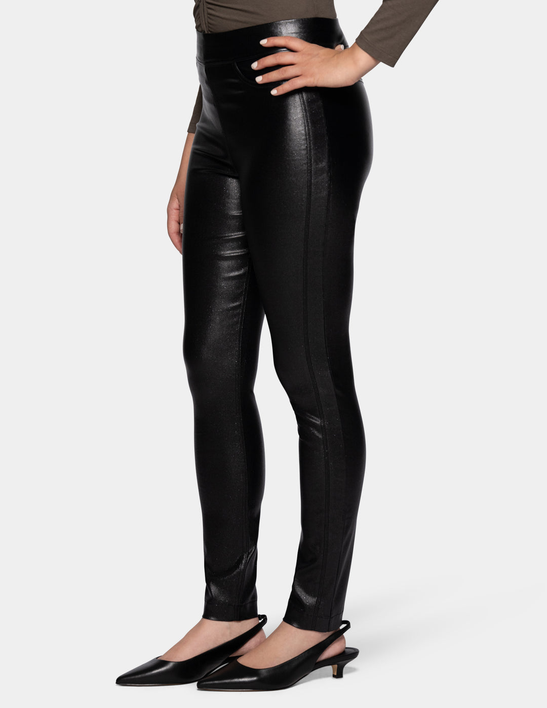 A sideview of a model wearing coated black pants, a grey 3/4 sleeve top, and black flats photographed against a light gray background.