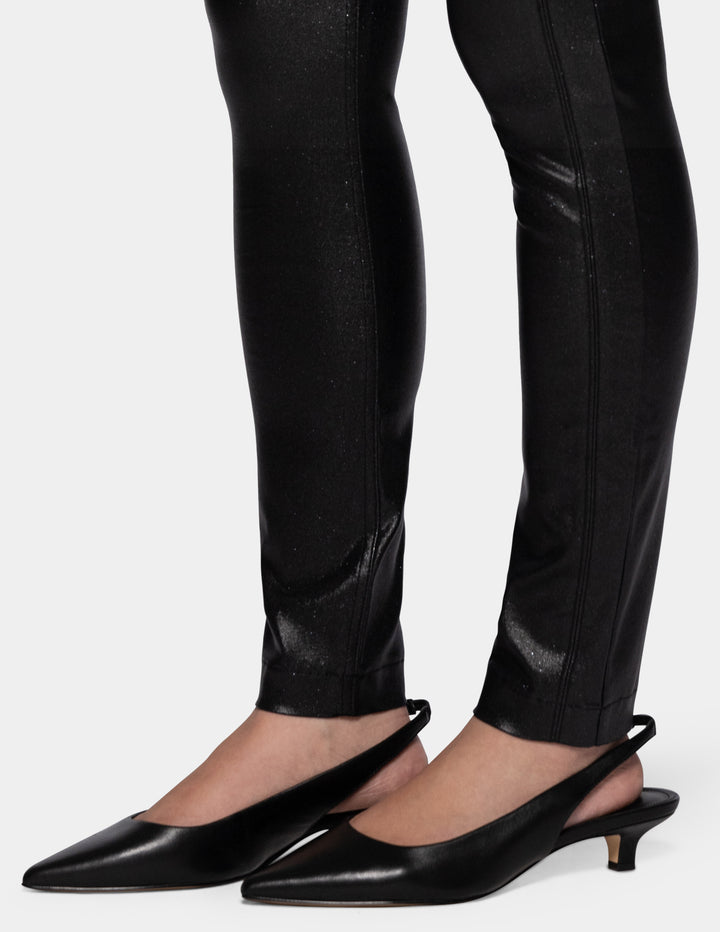 A model wearing coated black pants and black flats photographed against a light gray background.