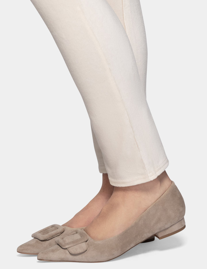A detailed view of an off white corduroy pant leg worn by a model, paired with beige colored flats