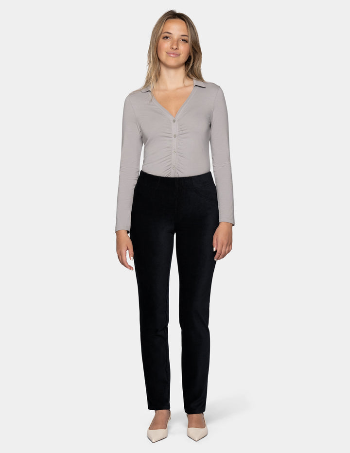 A model wearing black corduroy pants and a long sleeve grey top with ivory pointed toe shoes