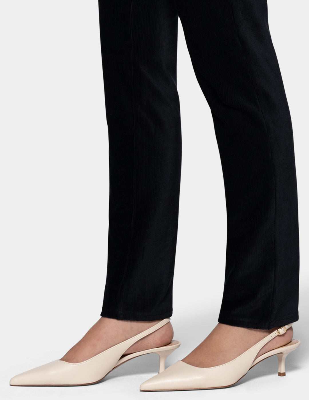 A model wearing black corduroy pants with ivory pointed toe shoes from the knee down