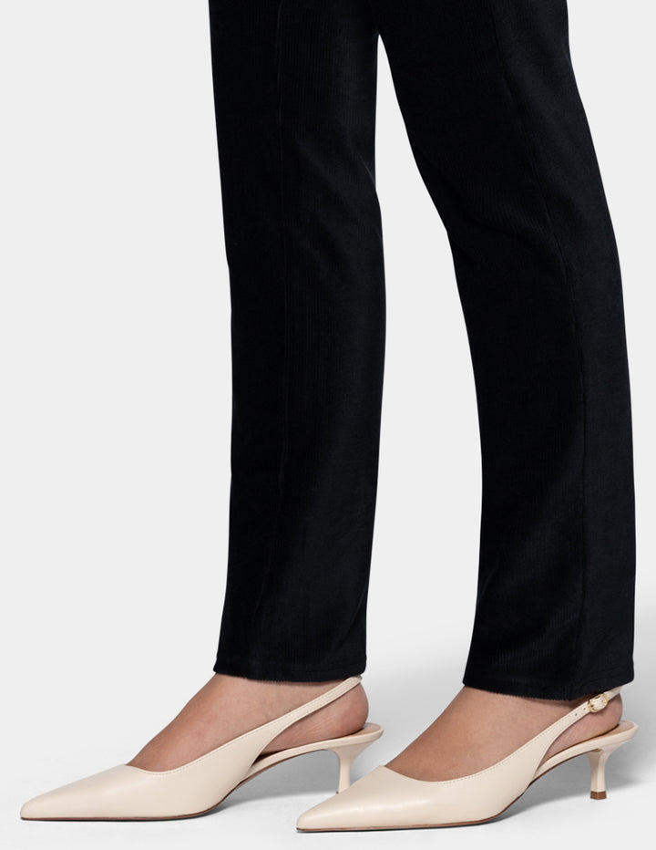 A model wearing black corduroy pants with ivory pointed toe shoes from the knee down