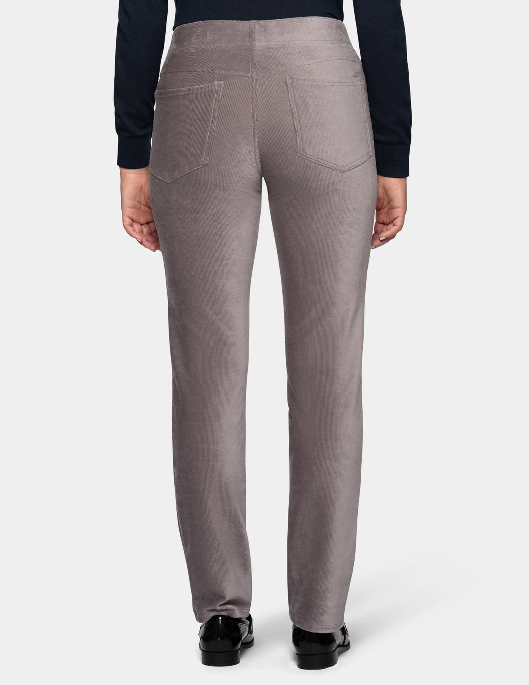 A backside view of a model wearing grey corduroy pants from the waist down with a long sleeve black top and black shoes