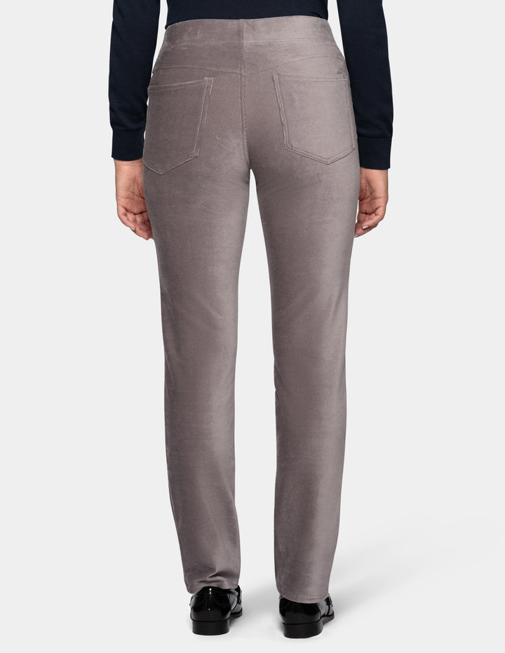 A backside view of a model wearing grey corduroy pants from the waist down with a long sleeve black top and black shoes