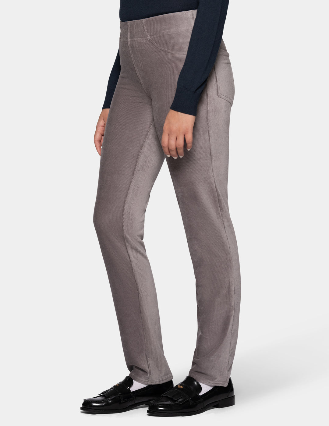 A sideview of a model wearing grey corduroy pants from the waist down with a long sleeve black top and black shoes