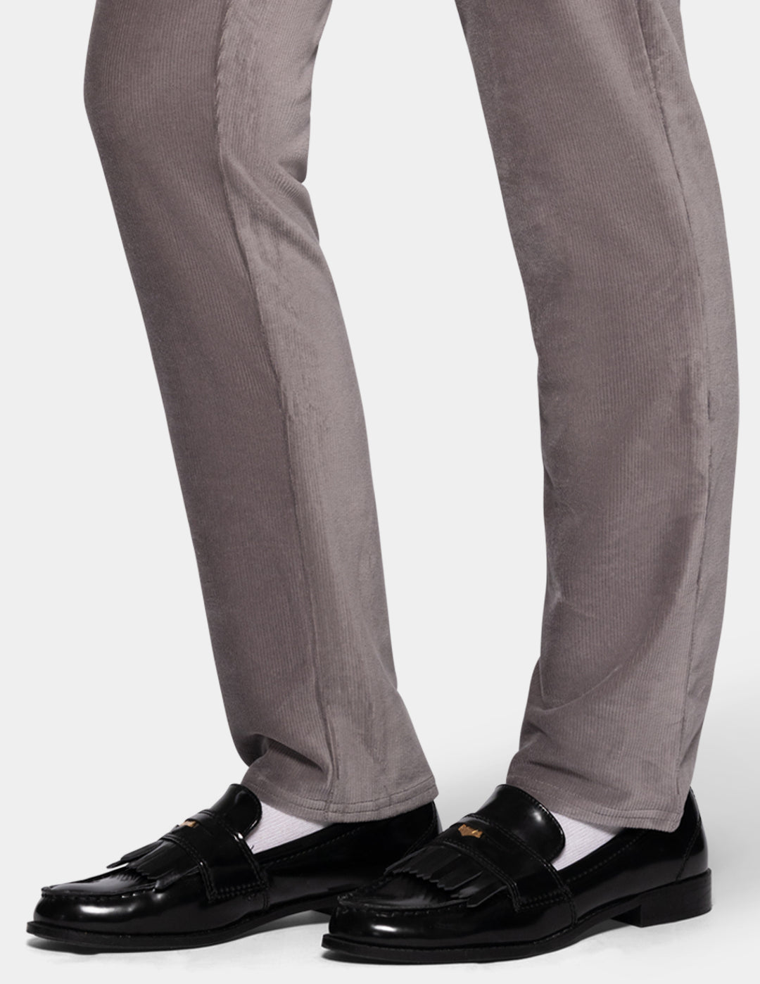 A detailed view of a model wearing grey corduroy pants from the knee down and black shoes