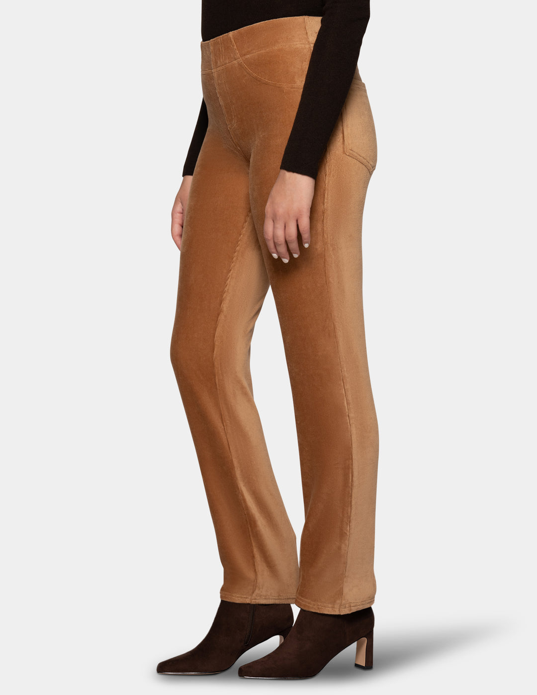 A side view of a model wearing tan corduroy pants with a long sleeve black top and dark brown boots