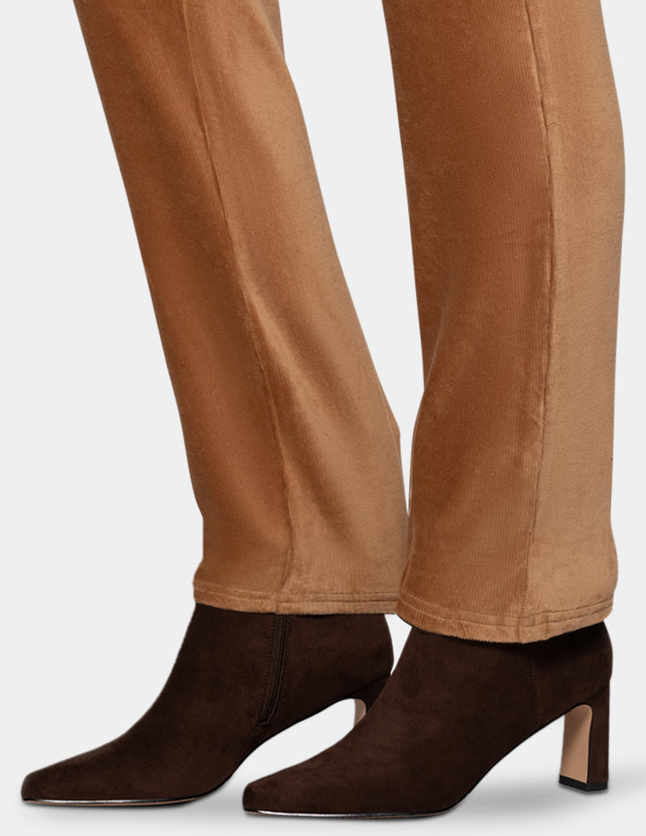 A detailed view of a model wearing tan corduroy pants and dark brown boots from the knee down