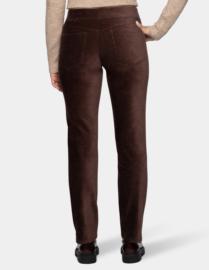 A backside view of a model wearing brown corduroy pants with a long sleeve beige cardigan and black shoes 