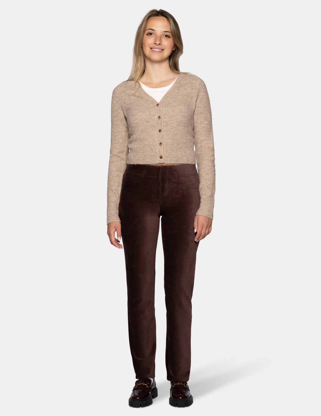 A model wearing brown corduroy pants with a long sleeve beige cardigan and black shoes 