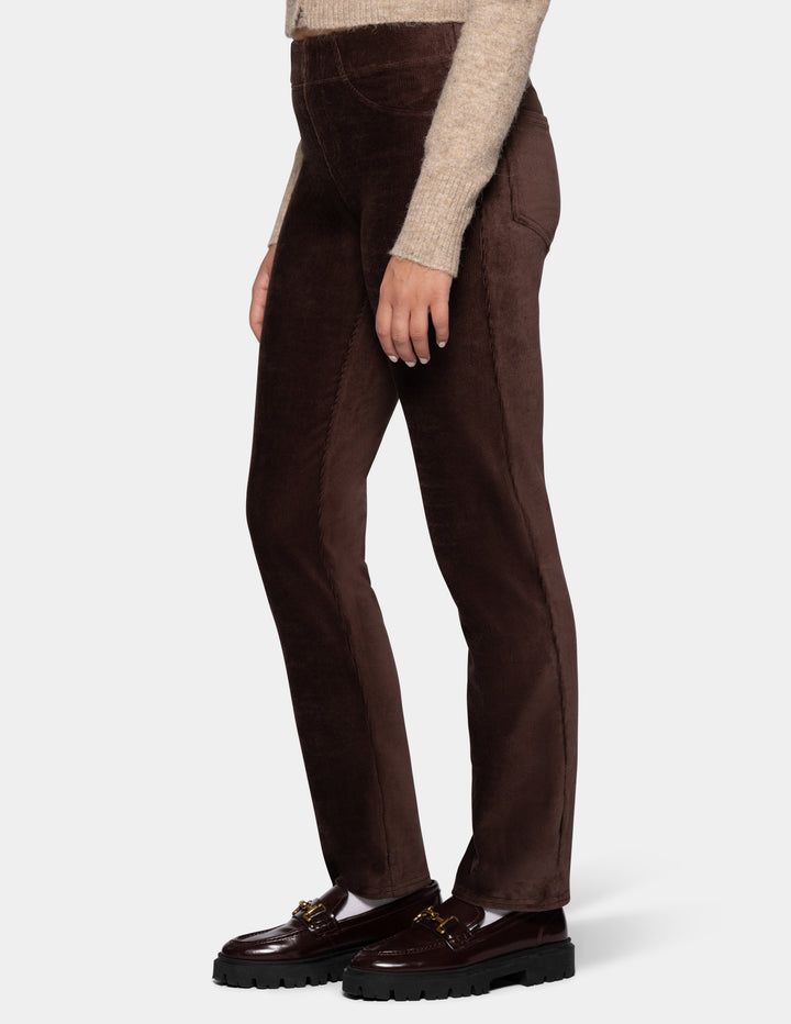 A side view of a model wearing brown corduroy pants with a long sleeve beige cardigan and black shoes 