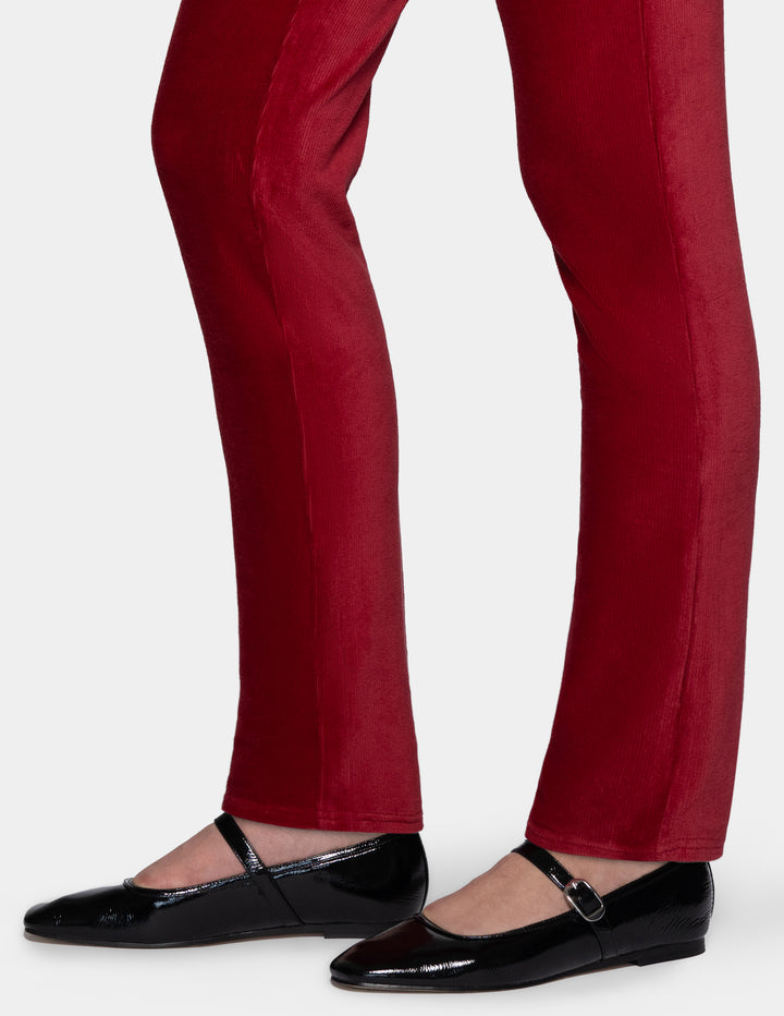 A detailed view of a model wearing red corduroy pants and black shoes from the knee down