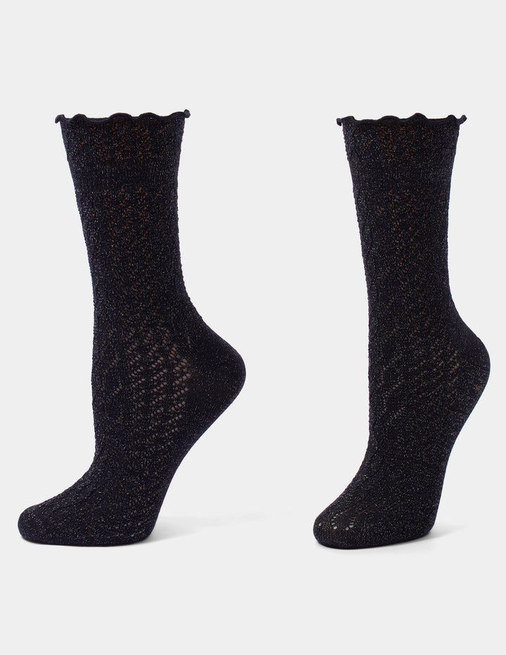 Black pointelle crew socks with metallic accents and a ruffle edge displayed against a light gray background.