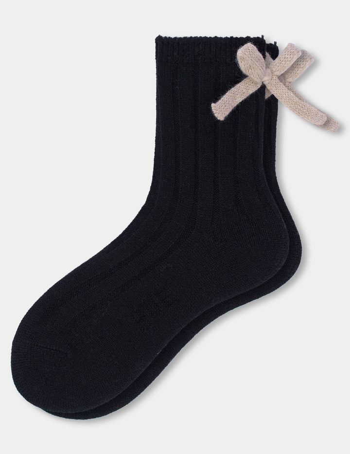 A black anklet sock with a beige bow accent photographed against a light gray background.