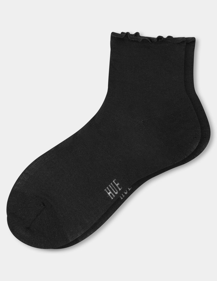 A pair of black ankle socks with a ruffled cuff, featuring the brand name 'HUE' printed in white near the heel, shown on a light gray background.