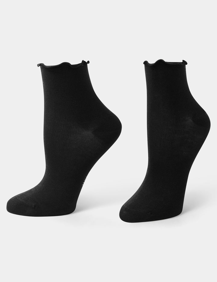 A pair of black ankle socks with a scalloped ruffle edge, displayed on foot forms against a light gray background.
