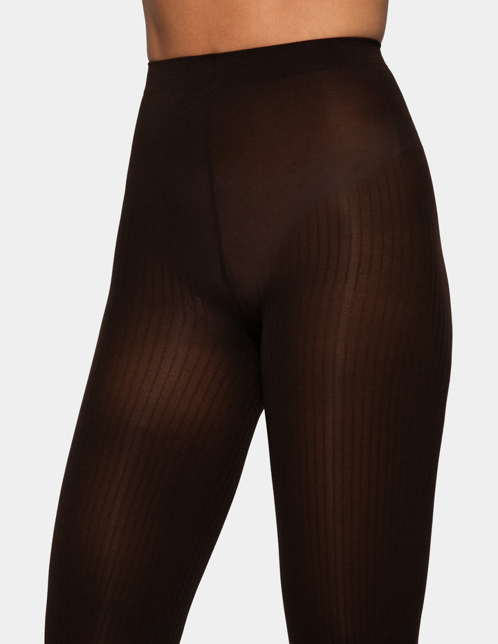 Close-up of a model wearing sheer ribbed tights in a very dark brown shade against a light gray studio background.