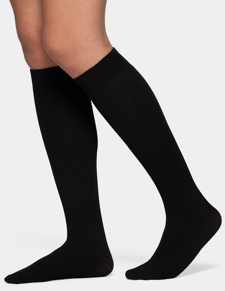 Black knee-high compression socks worn on a model's legs, shown against a plain light gray background.