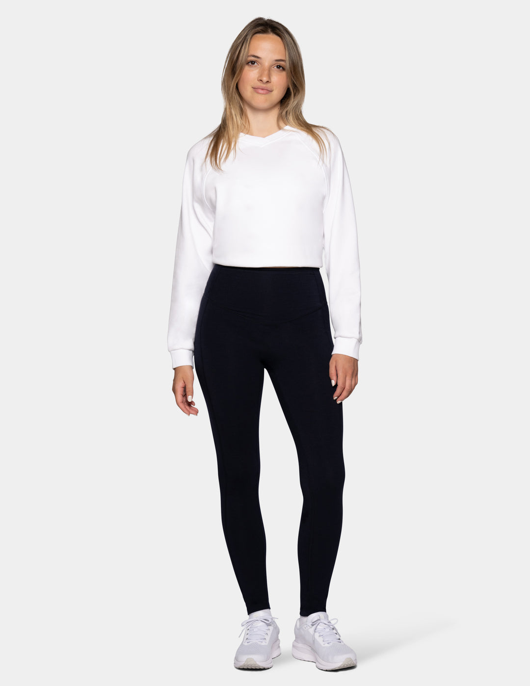 A model wearing navy leggings and a white sweater.