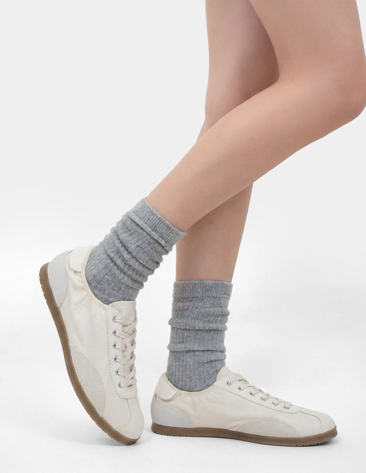 Person wearing gray socks and white sneakers on a light background