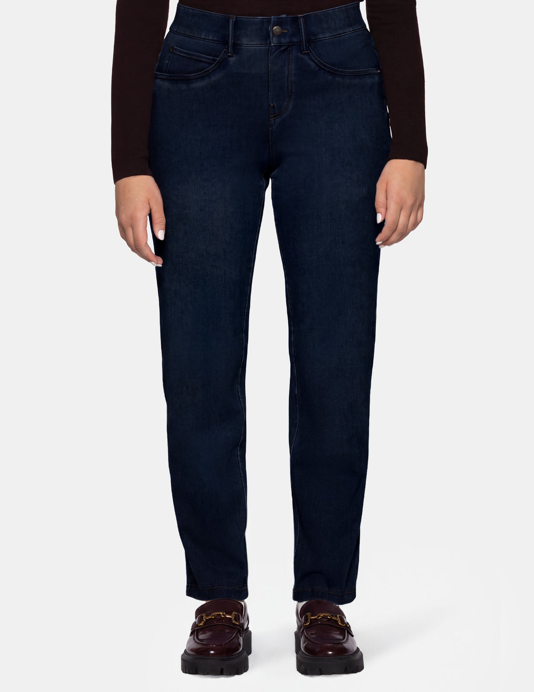 A model wearing dark blue denim pants, a long sleeve brown top, and brown loafers photographed against a light gray background.