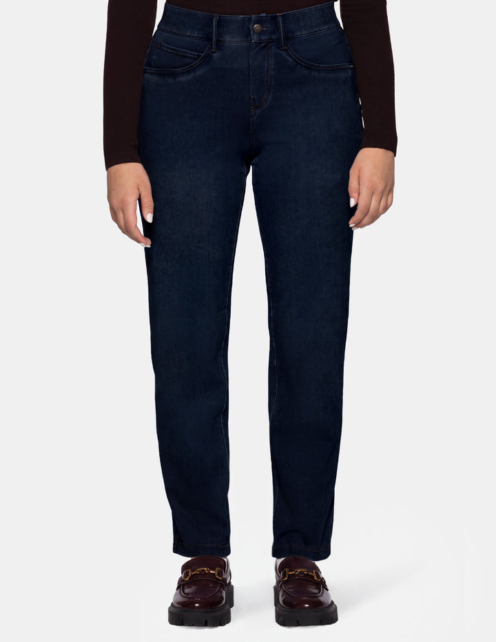A model wearing dark blue denim pants, a long sleeve brown top, and brown loafers photographed against a light gray background.