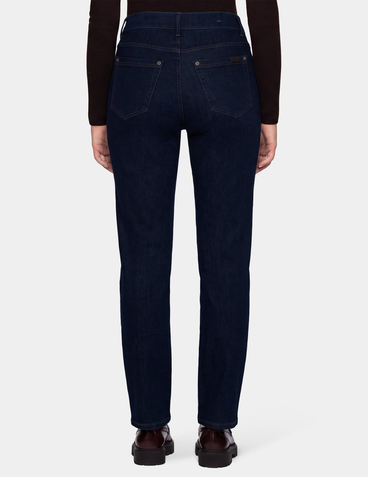 The back view of a model wearing dark blue denim pants, a long sleeve brown top, and brown loafers photographed against a light gray background.
