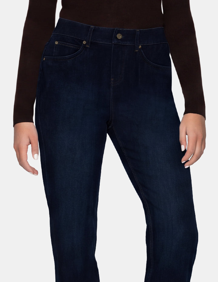 A model wearing dark blue denim pants and a long sleeve brown top photographed against a light gray background.