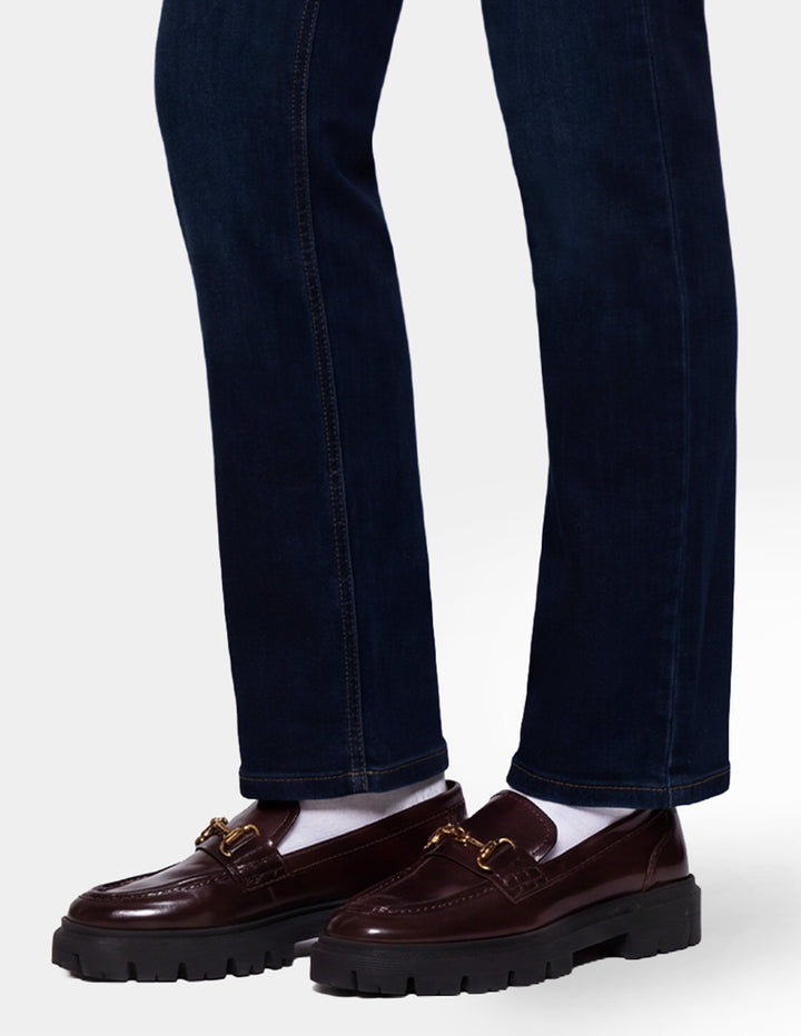 A model wearing dark blue denim pants and brown loafers photographed against a light gray background.