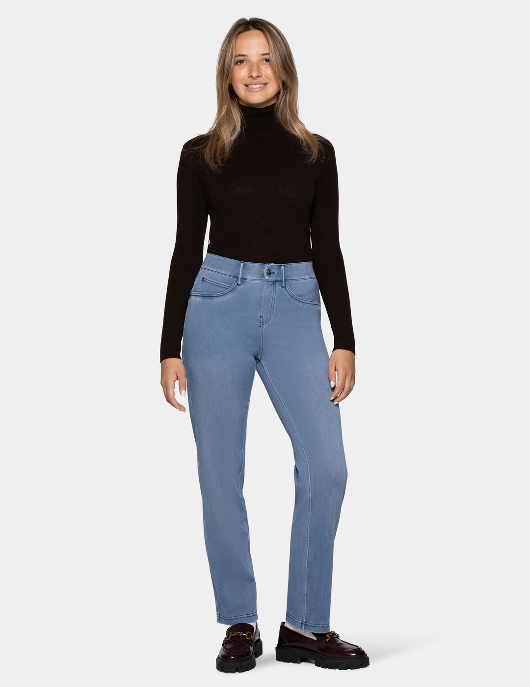 A model wearing light blue denim pants, a long sleeve black top, and loafers photographed against a light gray background.