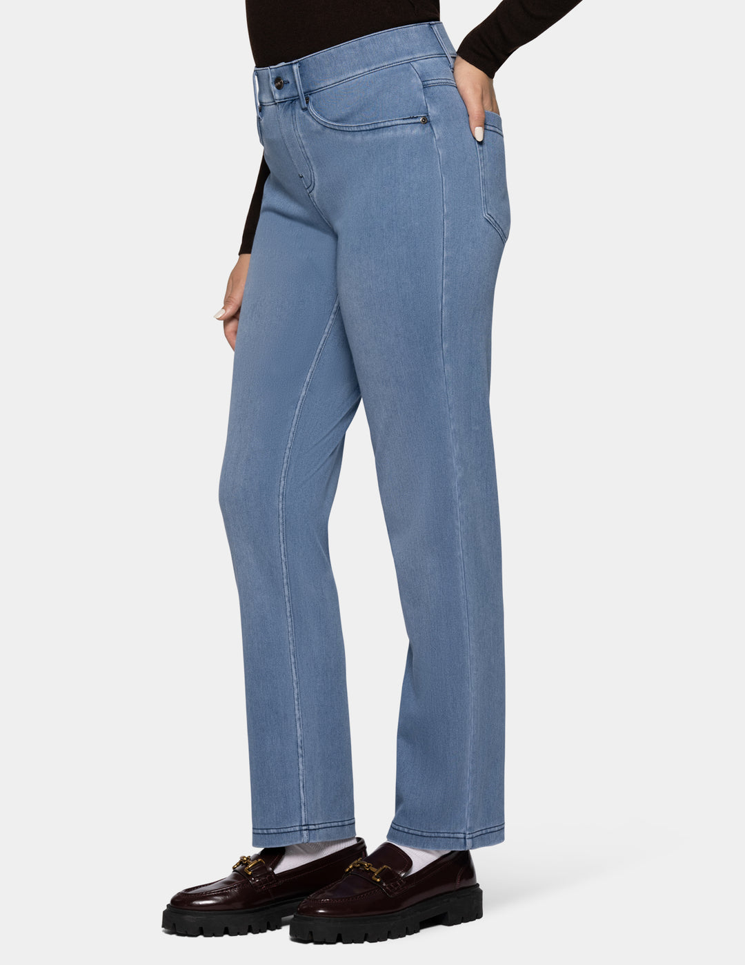 A sideview of a model wearing light blue denim pants, a long sleeve black top, and loafers photographed against a light gray background.